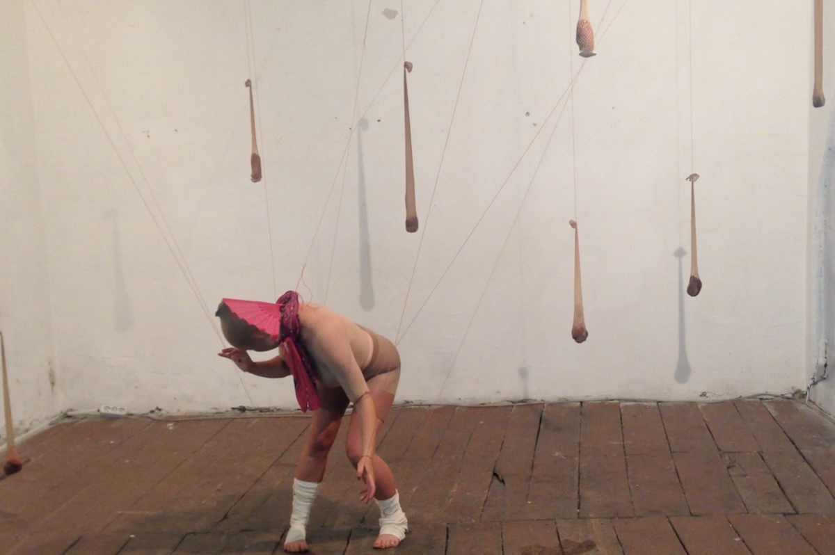 Performer bending beneath suspended organic forms in Body of a Home