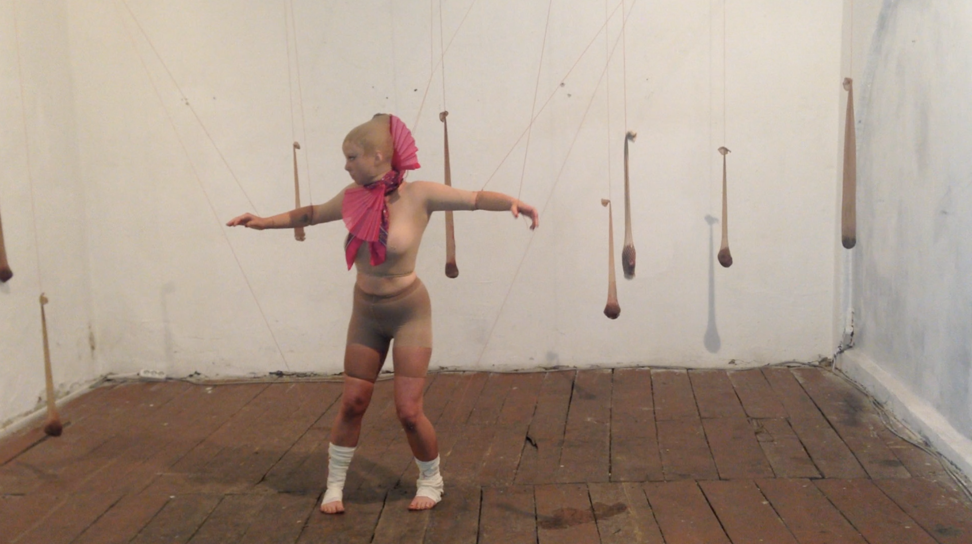 Performer extending both arms among suspended forms in Body of a Home