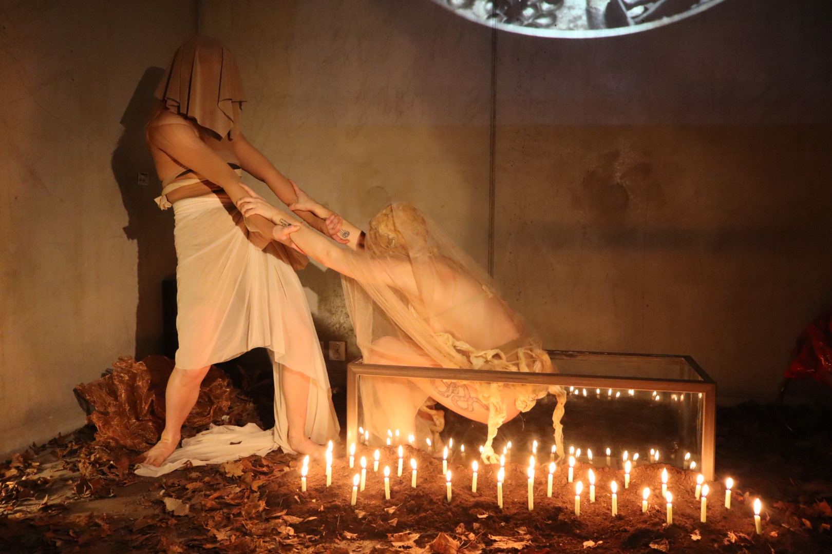 Two performers reaching toward one another beside a candle-filled glass case in Midnight Mass
