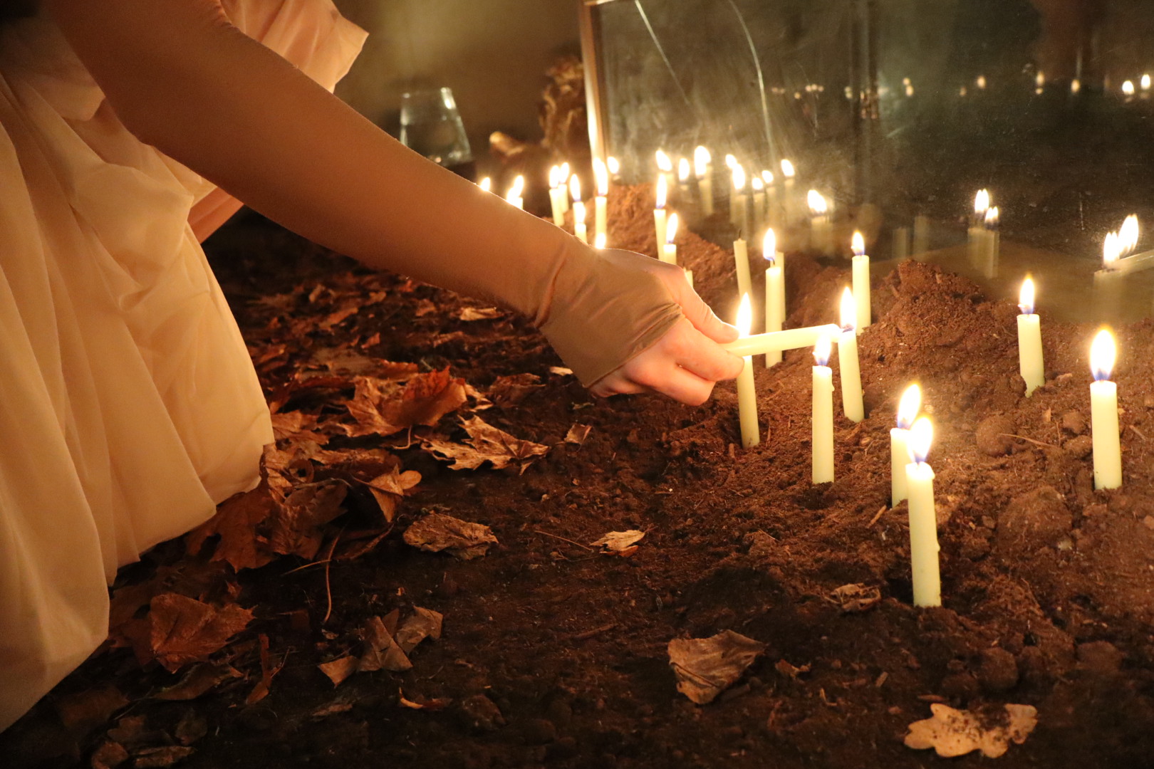 Performer lighting candles arranged in soil in Midnight Mass