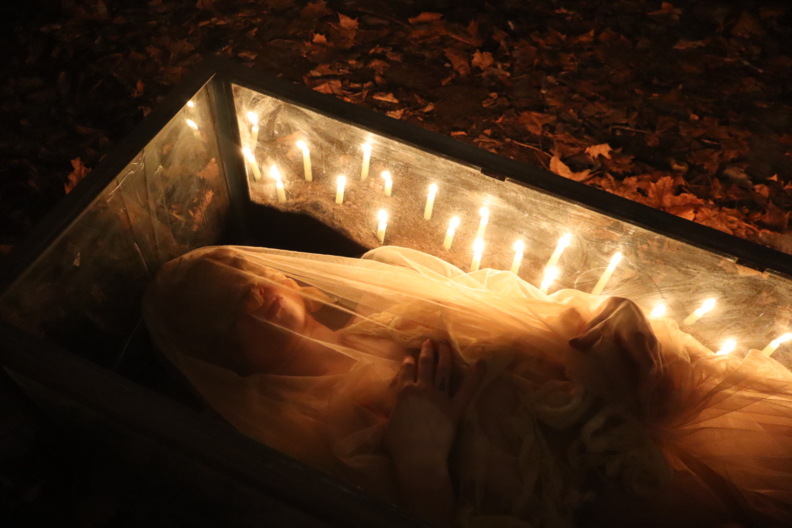 Performer lying beneath translucent fabric inside a candle-lit glass case in Midnight Mass