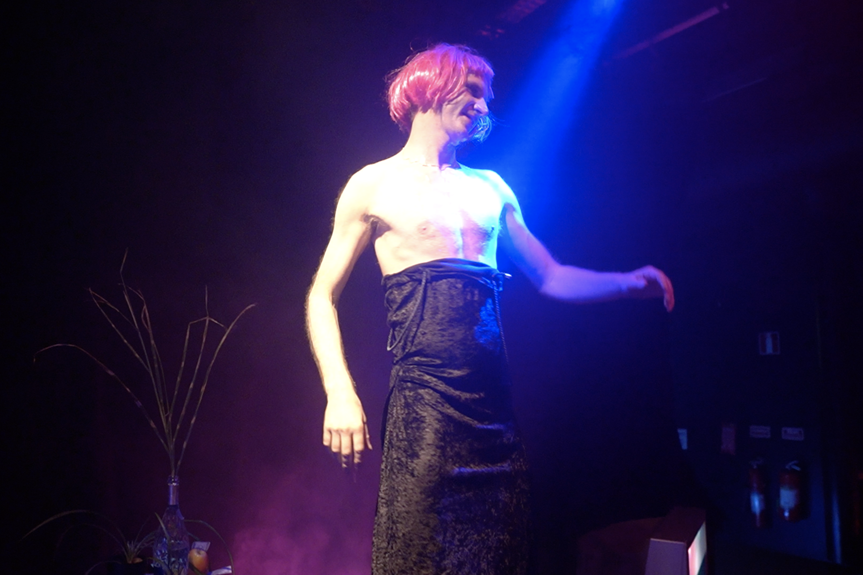 Performer standing under blue and red stage light in The Roost Social Club