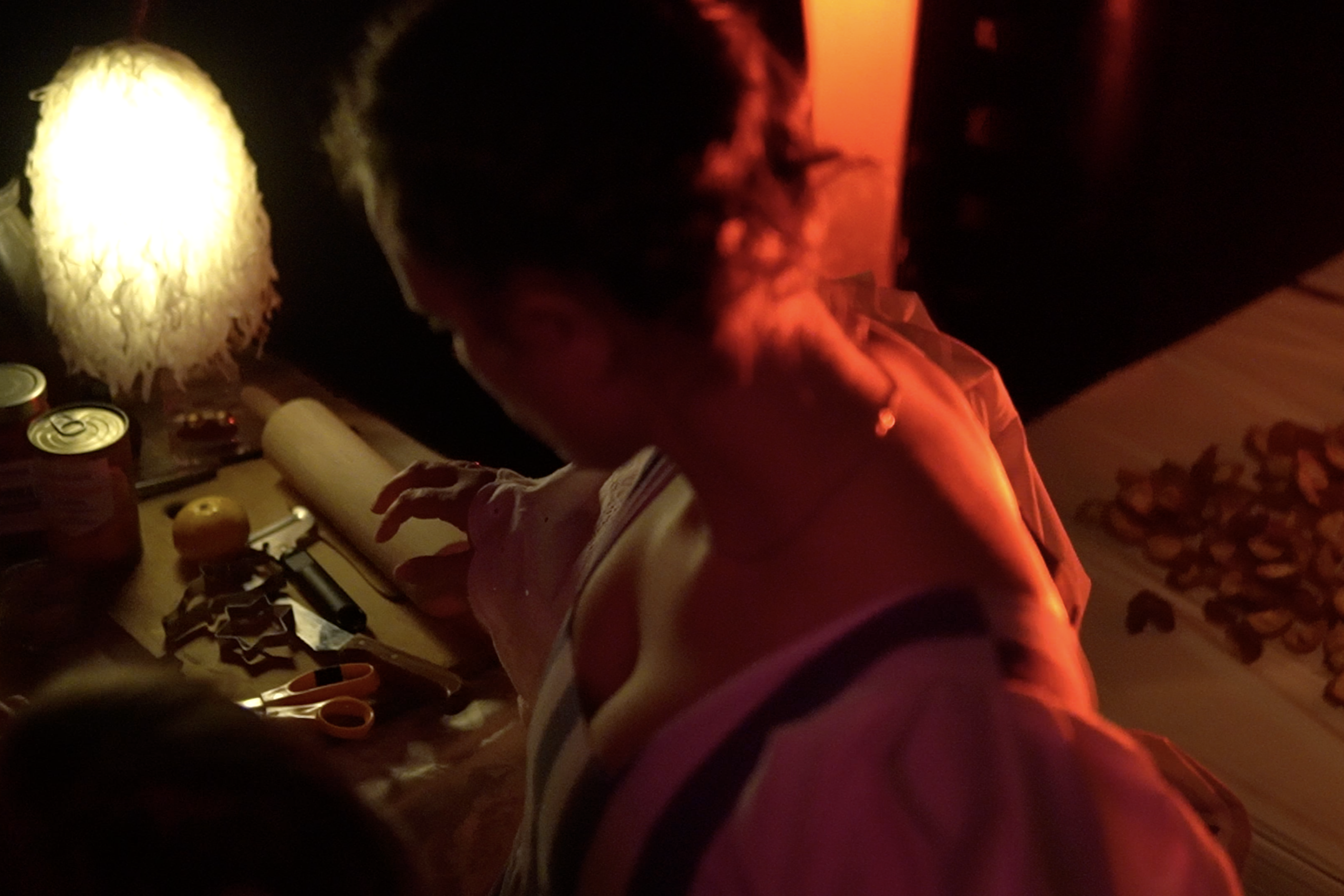 Performer seated at a table with masks and objects under red light in The Roost Social Club
