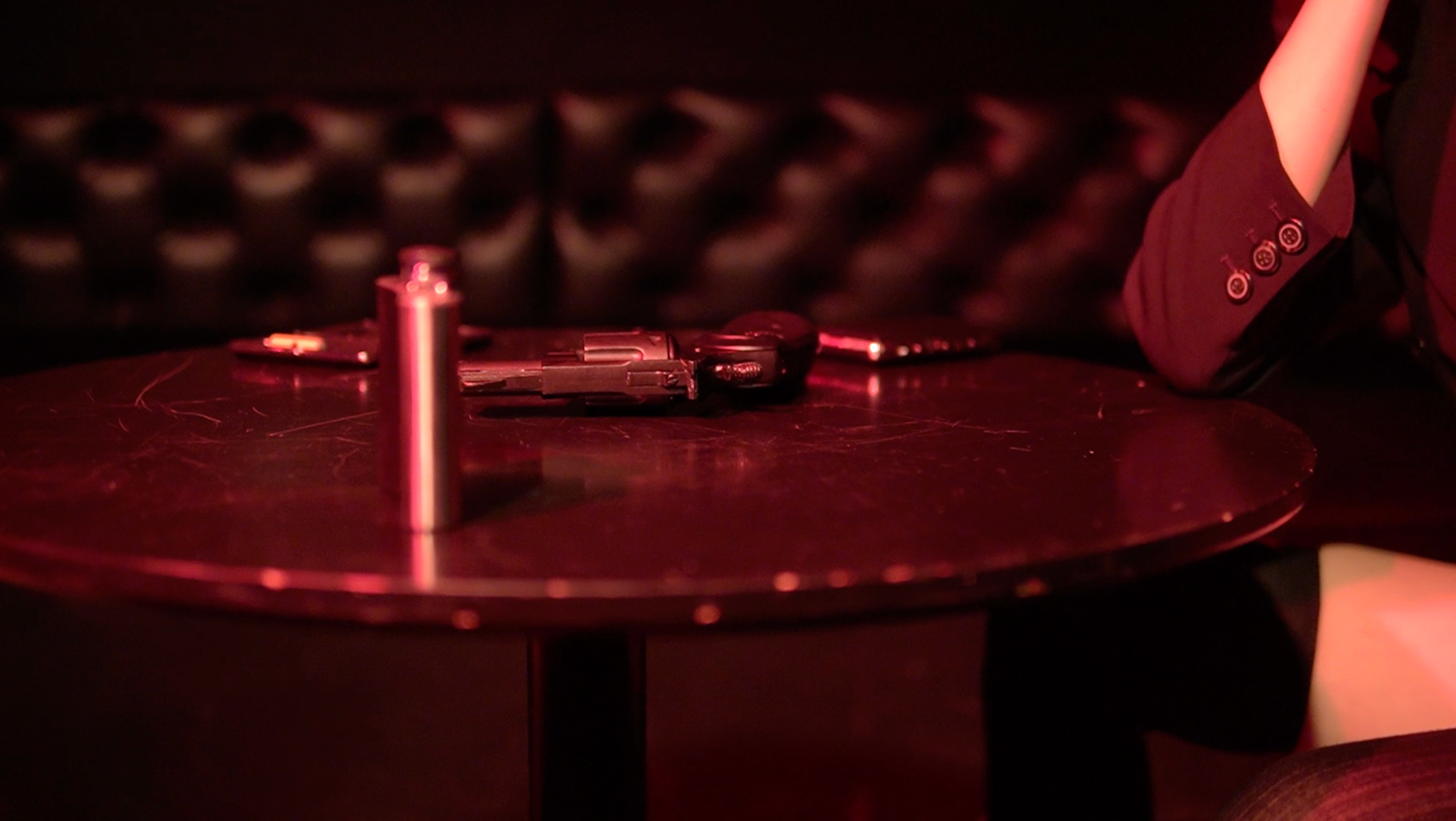 Red-lit table with a prop gun in The Roost Social Club